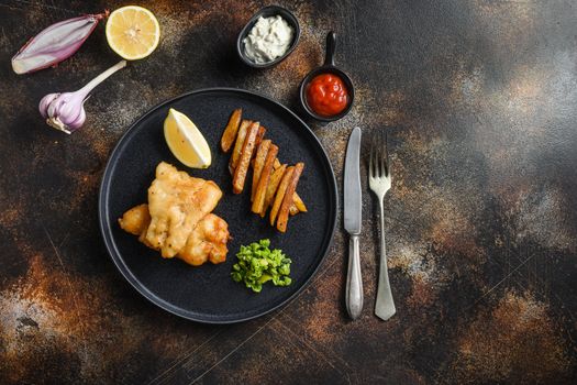 fish and chips with beer-battered cod and fries and a side of tartar sauce and mushy peas on black plate over old rustic metal style background top view space for text or recipe.