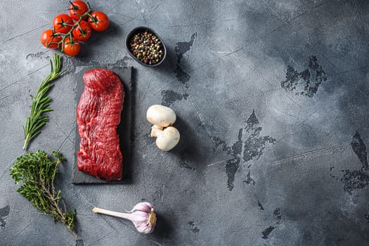Organic Tri-tip, triangle roast marbled beef on black plate , marbled beef with herbs tomatoes peppercorns over grey stone surface background top view Space for text.