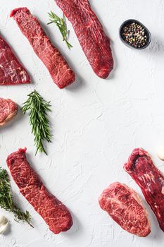 Set of different alternative types of raw beef steaks,on a white stone background top view concept frame in corners space for text vertical in center.