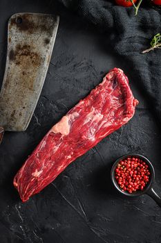 Raw machete also known as bistro steak, fajita meat or onglet, near butcher knife with pink pepper and rosemary. Black background. Top view. Vertical.