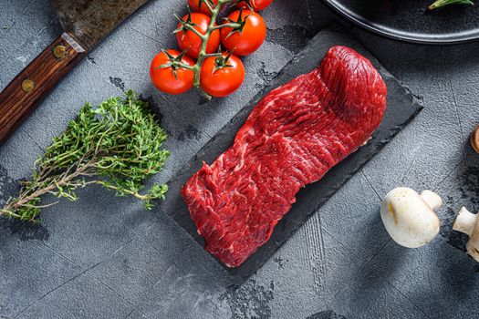 Raw tri tip, bottom sirloin cut steak on black slate raw organic food , marbled beef over other alternative cuts with herbs tomatoes peppercorns over grey stone surface background top view .