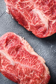 Raw top blade flat Ironcut, on black slate , bio marbled beef with herbs tomatoes peppercorns over grey stone surface background top view close up vertical.