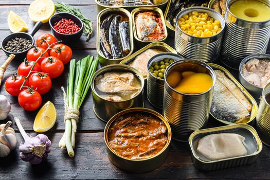 Different canned conserve products in tin cans. with fresh organic ingridients Saury, mackerel, sprats, sardines, pilchard, squid, tuna pinapple, corn, peas, mango , beans, over old wood dark textured background side view.