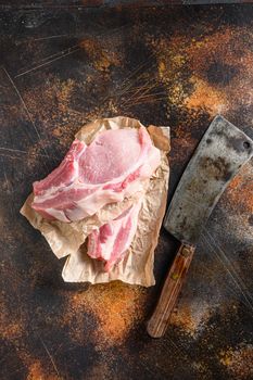 Raw pork chop warped in paper with butcher cleaver inside over rustic metall table top view vertical.