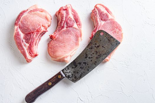 Butcher cleaver over organic bio Raw pork chops set for grilling, baking or frying, textured white background. horizontal.