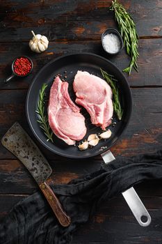 Fresh raw pork meat on frying grill pan with butcher knife or cleaver and ingedients for grill top view vertical over old wood dark background.