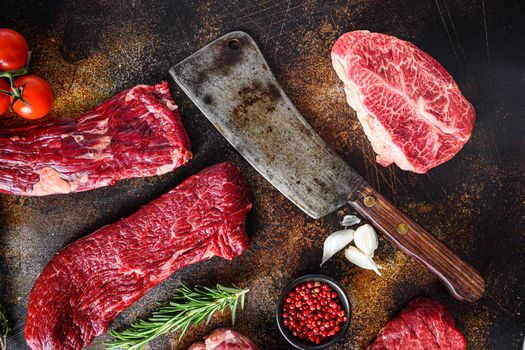 Butcher cleaver knife with set of different alternative types of raw beef steaks on a rustic metall background top view layflat.