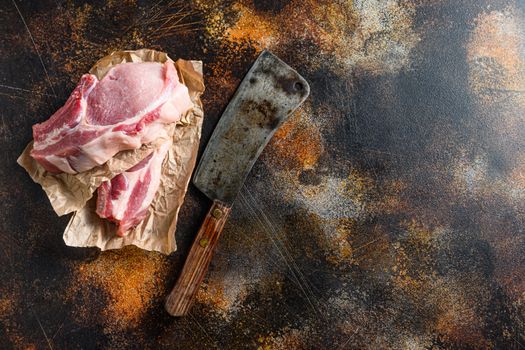 Raw pork chop warped in paper with butcher cleaver inside over rustic metall table top view space for text.