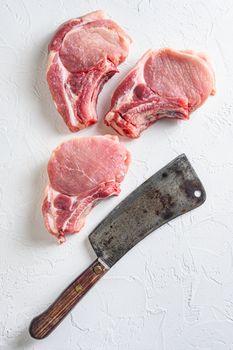 Organic bio Raw pork chops set for grilling, baking or frying, Fith butcher cleaver ower textured white background. Overhead view.