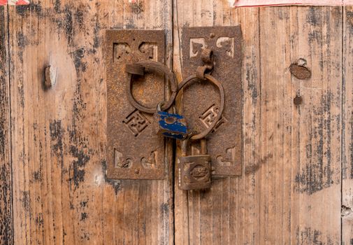 Rusty padlocks link the circular iron handles on wooden doors in ancient chinese doorway