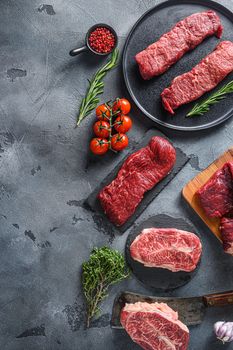 Organic denver, top blade, tri tip steak on a black plate and stone slate with seasonings, herbs grey concrete background. Top view vertical concept space for text.