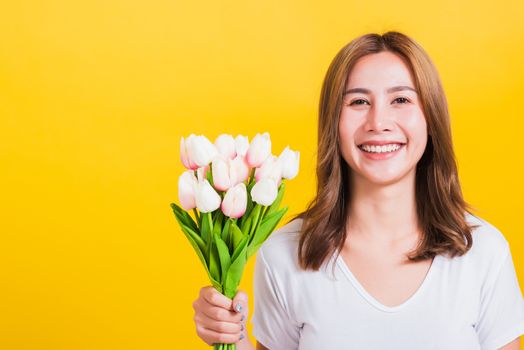 Portrait Asian Thai beautiful happy young woman smiling, screaming excited hold flowers tulips bouquet in hands and looking to camera, studio shot isolated on yellow background, with copy space