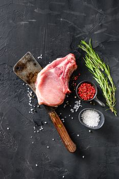Organic cutlet on a rib or Pork meat over american classic butcher knife or cleaver with spices and rosemary and red pepper on black slate top view. vertical.