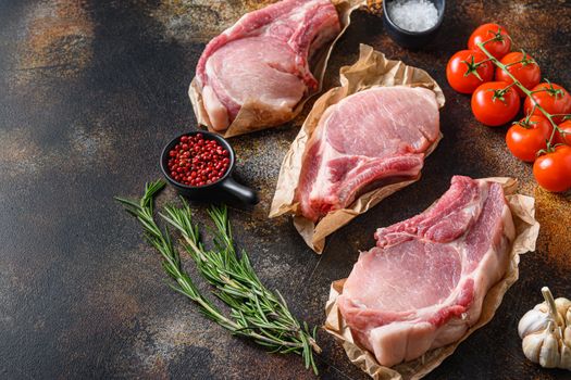 Tree bunch raw pork chops arranged with herbs, oil and spices. Cooking meat. On dark background with space for text.