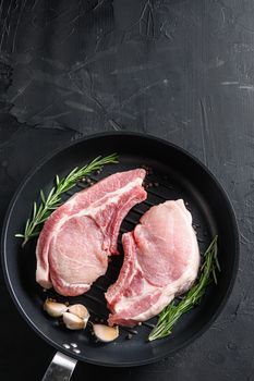 pork rib chops in frying pan grill skillet with herbs, spices top view black stone bakground space for text vertical.