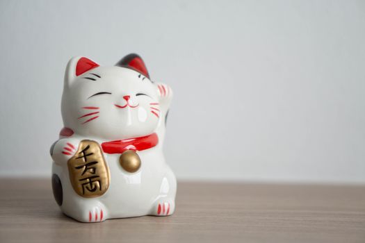 Maneki neko lucky cat show text on hand meaning rich on wood table background, select focus