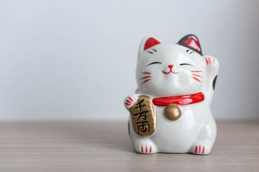 Maneki neko lucky cat show text on hand meaning rich on wood table background, select focus