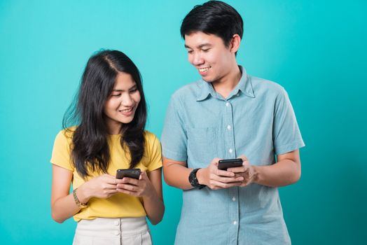 Portrait happy Asian young handsome man, beautiful woman couple smile standing wear shirt, excited young couple holding mobile phones looking at cellphone, studio shot on blue background