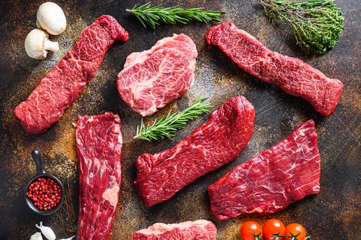 Organic set of raw alternative beef steaks flap flank Steak, machete steak or skirt cut, Top blade or flat iron beef and tri tip, triangle roast with denver cut side view over old rustic metal surface .