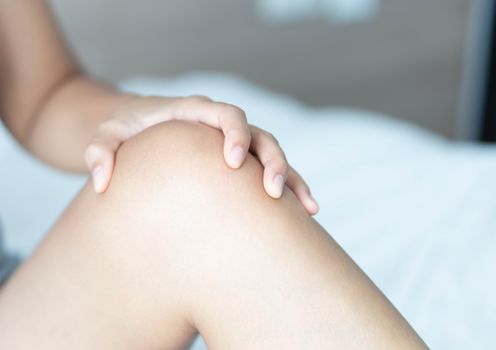 Closeup woman hand holding knee with pain on bed, health care and medical concept