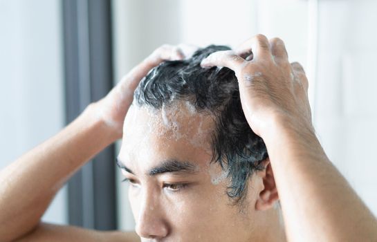 Closeup young man washing hair with with shampoo in the bathroom, health care concept, selective focus