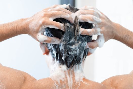 Closeup young man washing hair with with shampoo in the bathroom, health care concept, selective focus
