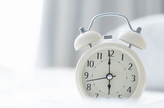 Alarm clock on white bad with light from window, selective focus