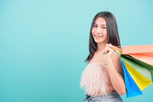 Asian happy portrait beautiful young woman standing smile in summer shopping her holding multicolor shopping bags on hand and looking to camera on blue background with copy space for text