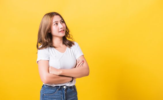 Asian Thai happy portrait beautiful cute young woman standing wear t-shirt her smile confidence with crossed arms looking to side up isolated, studio shot on yellow background and copy space