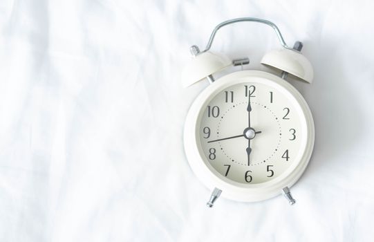 Close up alarm clock on white bed, selective focus