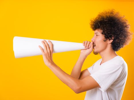 Asian handsome man with curly hair he announcing or spreading news using white speaker paper isolate on yellow background