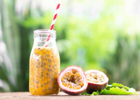 Glass bottle of passion fruit juice wood table with green nature background, food healthy concept