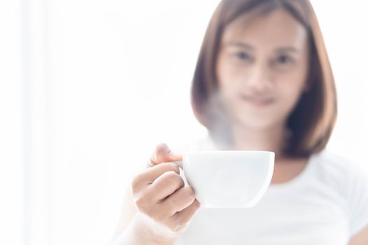 Closeup woman holding a cup of hot coffee with over light from window, selective focus