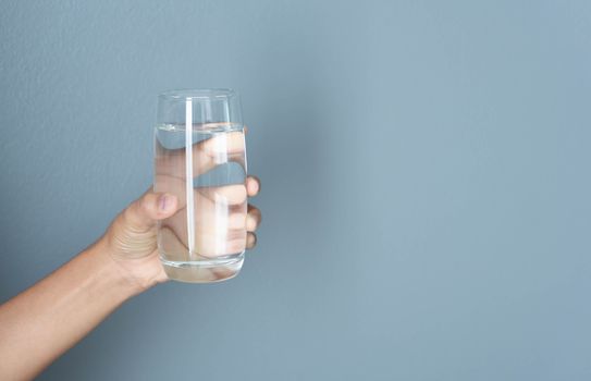Close up woman hand holding a glass of pure water for dink with grey background, Health care concept