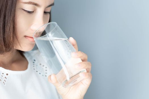 Closeup asian woman drinking pure water with grey background, health care concept, selective focus