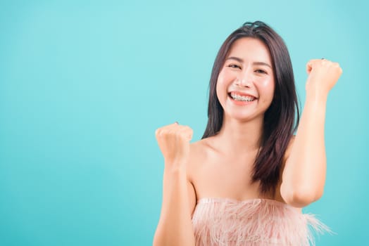 Smiling face Asian beautiful woman her celebrating success looking to camera on blue background, with copy space for text