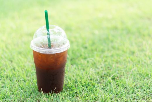 Close up glass of ice americano coffee with green grass nature background, selective focus