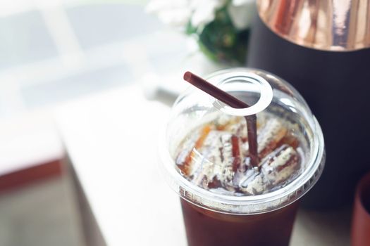 Close up ice of americano on wood table background with flower pot in coffee shop 