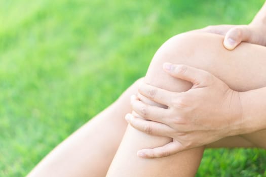 Closeup woman hand holding knee with pain on green grass, health care and medical concept