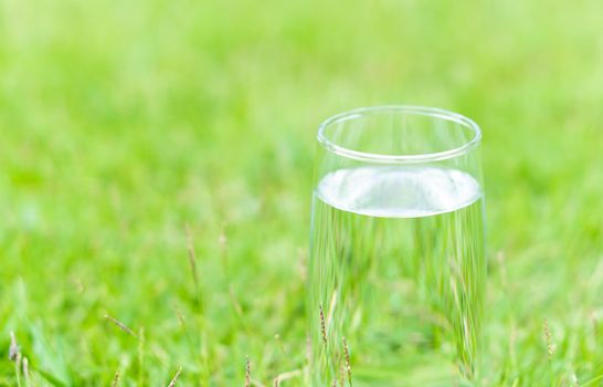 Closeup glass of water on green grass nature background, food healthy concept