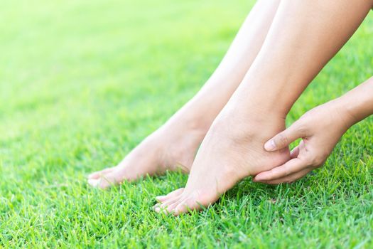 Woman hand holding foot with pain on green grass nature background, health care and medical concept