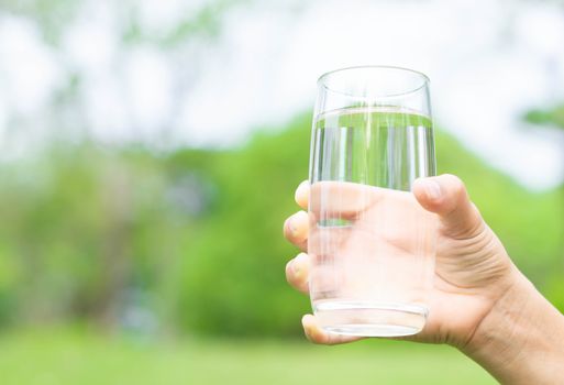 Hand holding glass of pure water on green nature background, healthy concept 