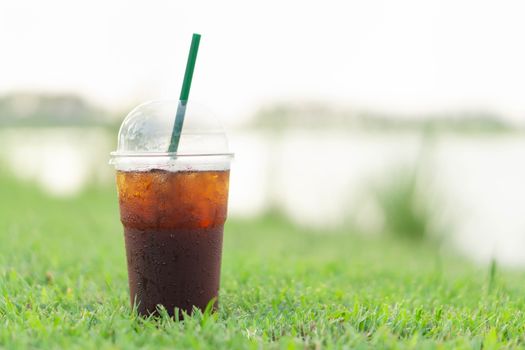 Close up glass of ice americano coffee with green grass nature background, selective focus