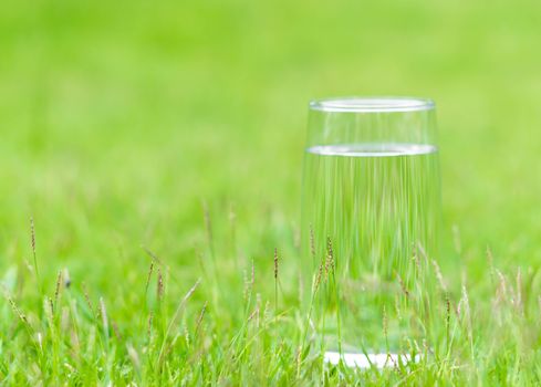 Closeup glass of water on green grass nature background, food healthy concept