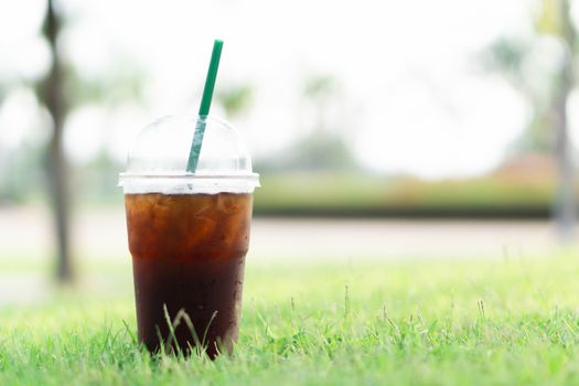 Close up glass of ice americano coffee with green grass nature background, selective focus  