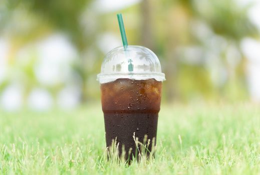 Close up glass of ice americano coffee with green grass nature background, selective focus  