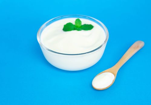 Close up yogurt  in glass bowl  with wooden spoon on blue background