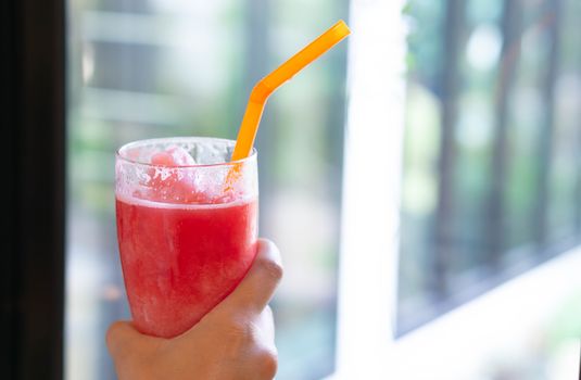 Closeup hand holding watermelon smoothie with green nature background, selective focus