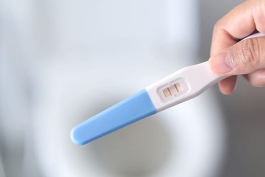 Closeup woman hand holding pregnancy test in bathroom, health care concept, selective focus