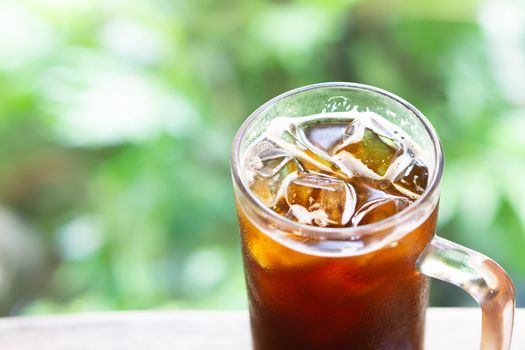 Closeup glass of ice americano coffee with green nature background, selective focus